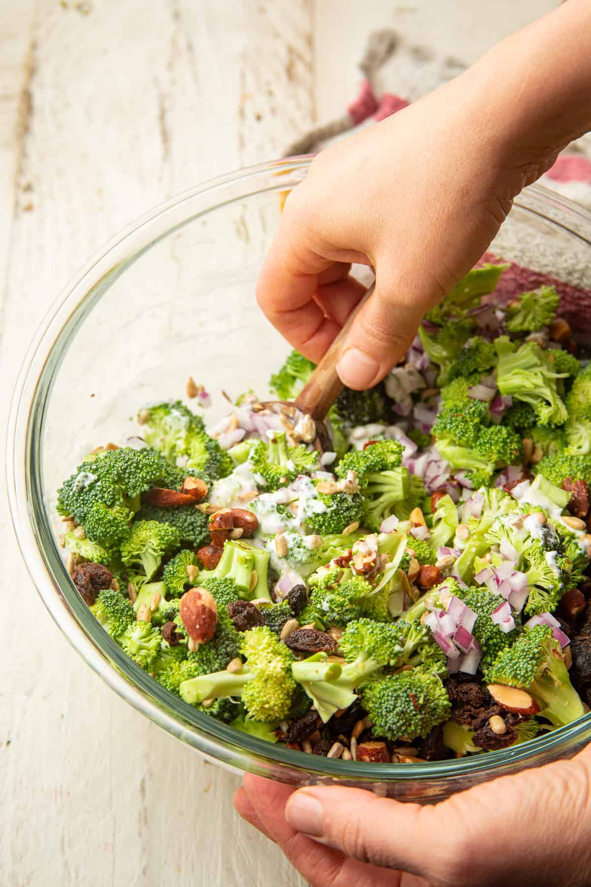 Hand stirring Vegan Broccoli Salad together in a glass bowl.
