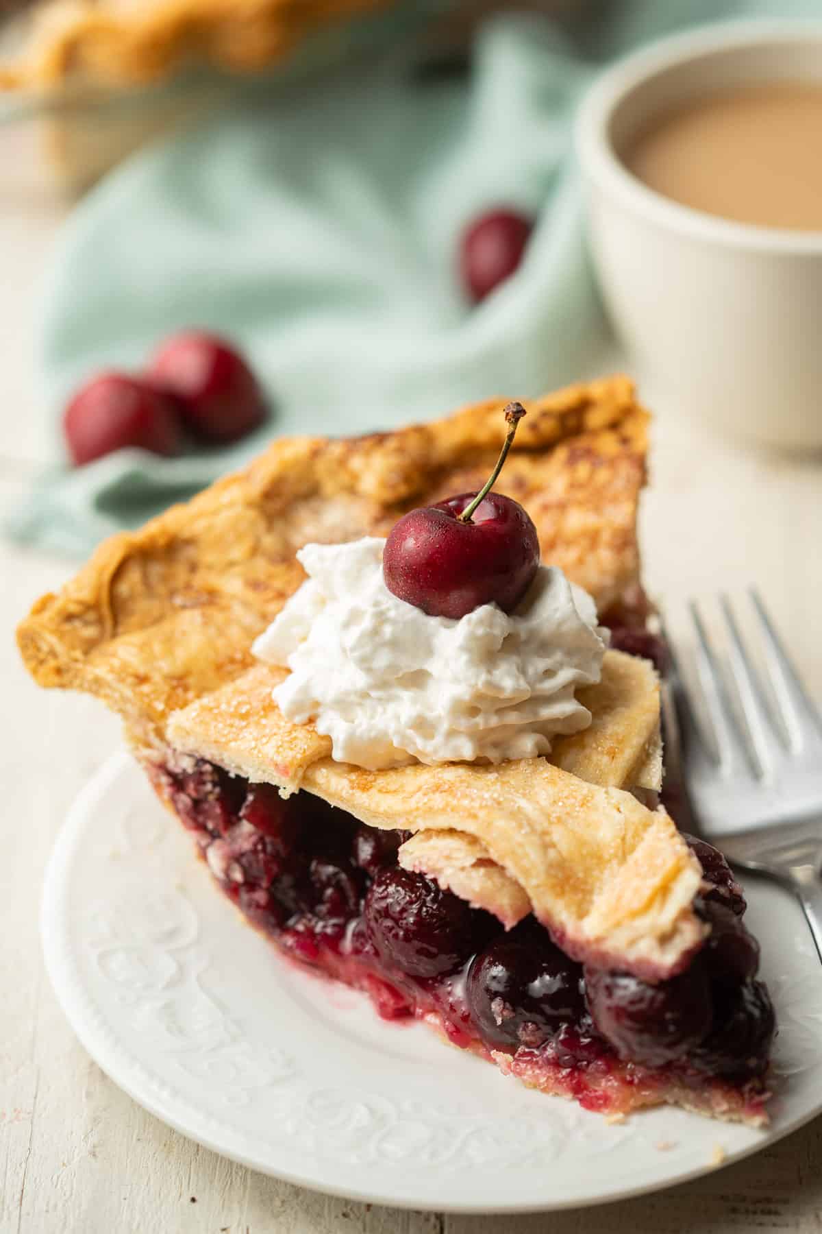 Slice of Vegan Cherry Pie on a plate with coffee cup and napkin in the background.