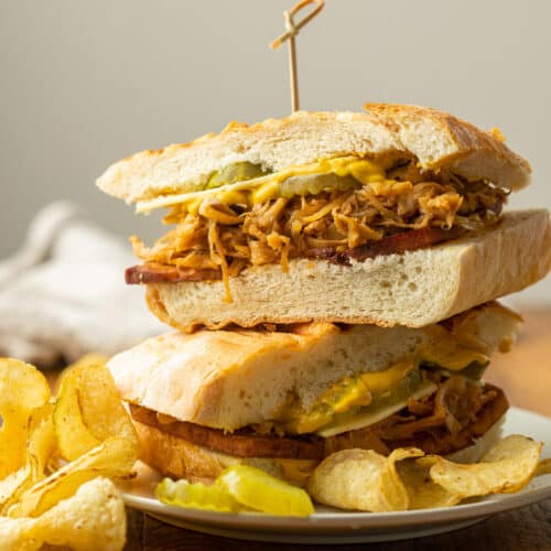 Two Vegan Cuban Sandwiches stacked on top of each other on a plate with potato chips.
