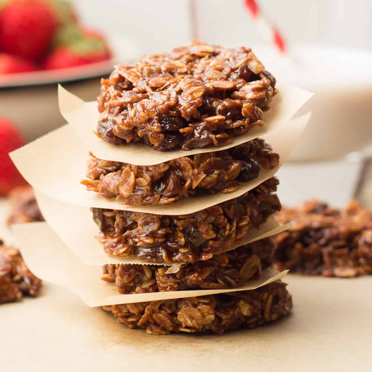 Stack of Vegan No Bake Cookies with strawberries and glass of almond milk in the background.