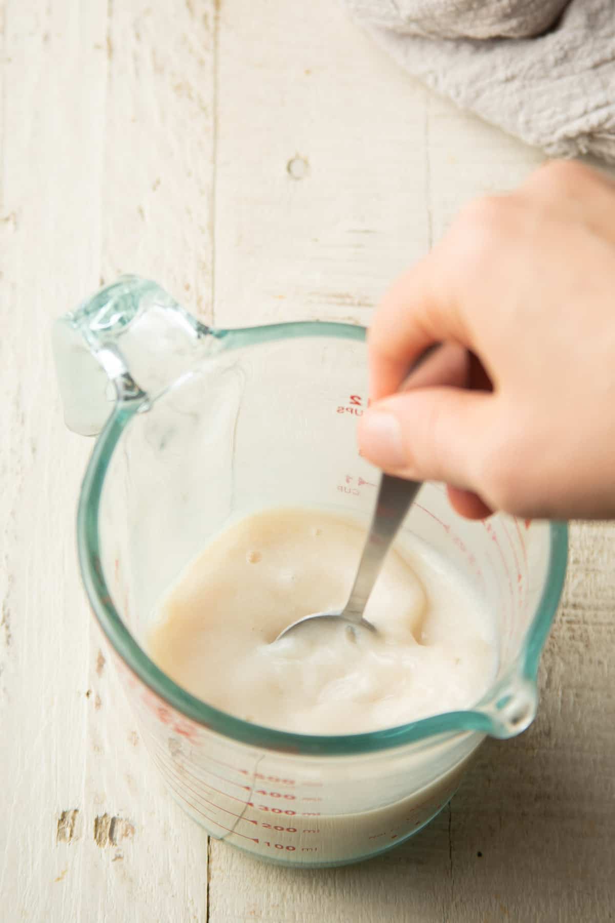 Hand stirring liquid ingredients for cake batter together in a liquid measuring cup.