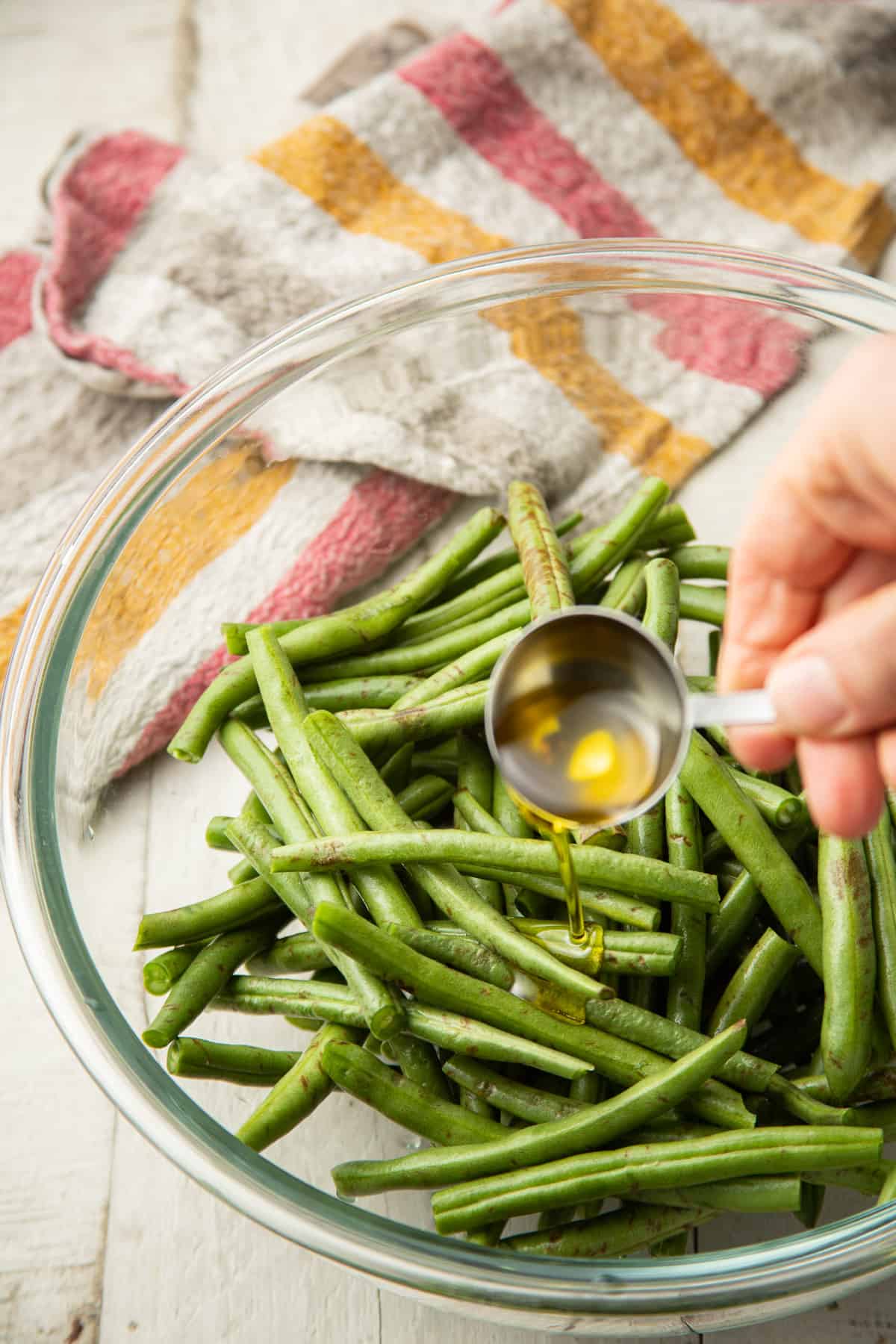 Hand drizzling olive oil into a bowl of green beans.