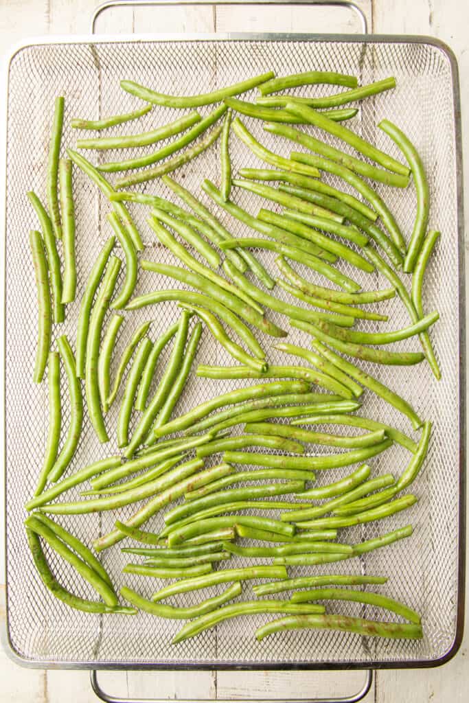 Green beans arranged in a single layer in air fryer basket.