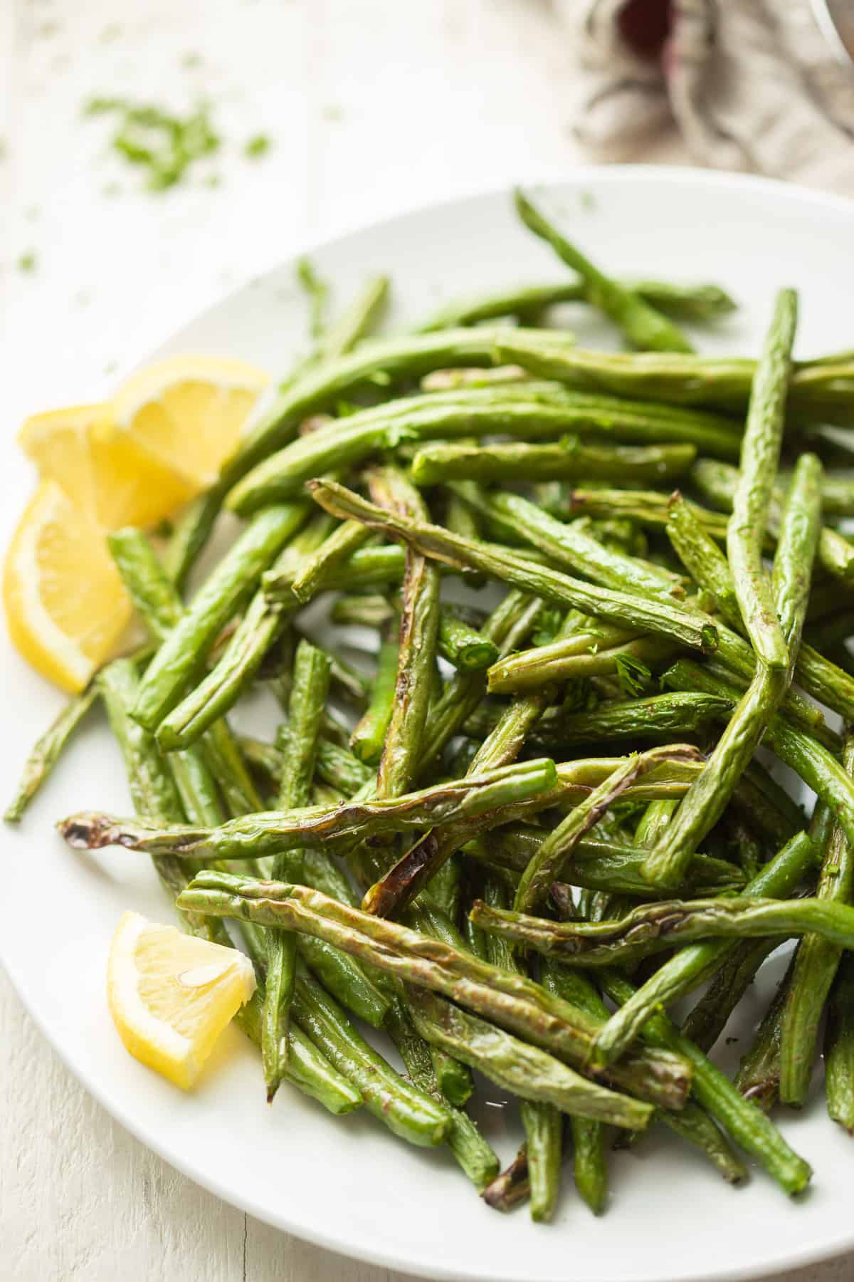 Close up of air fried green beans on a plate with lemon wedges.