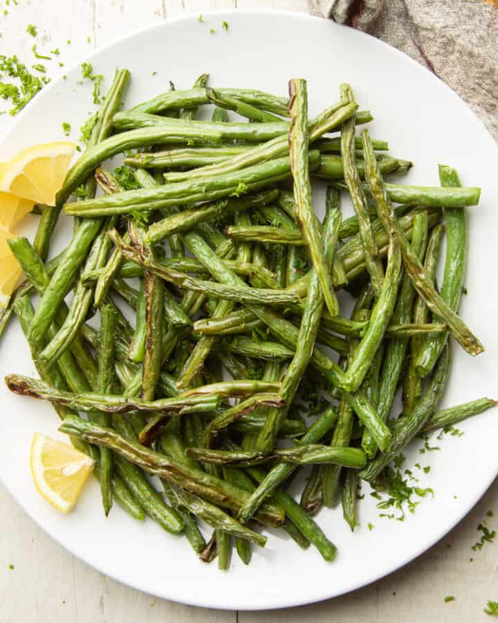 Plate of air fried green beans with lemon wedges.