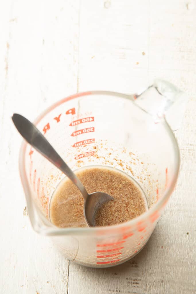 Flaxseed and water in a liquid measuring cup with spoon.