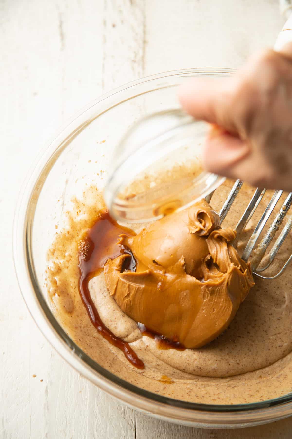 Hand adding cookie butter and vanilla to a mixing bowl.