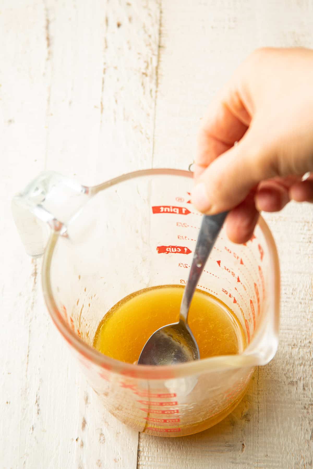 Hand stirring lime dressing ingredients together in a liquid measuring cup.