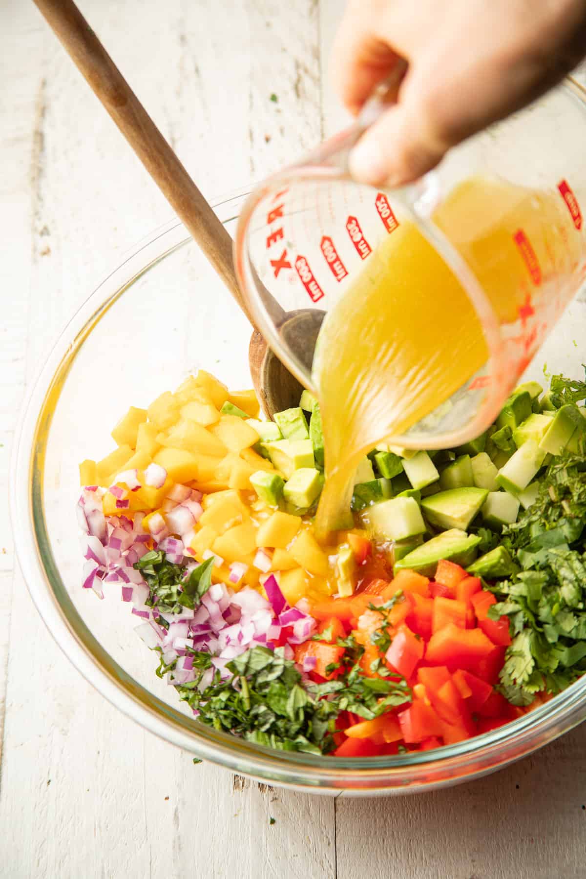 Hand pouring dressing over a bowl of mango salad.