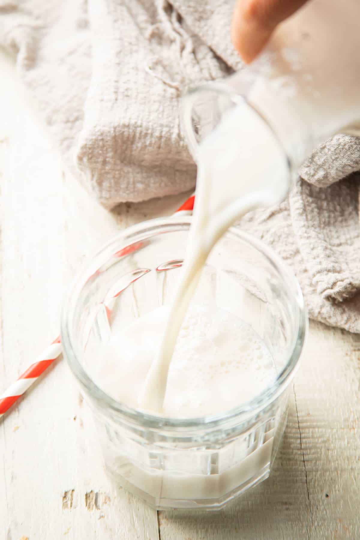 Plant based milk being poured from a jug into a glass.