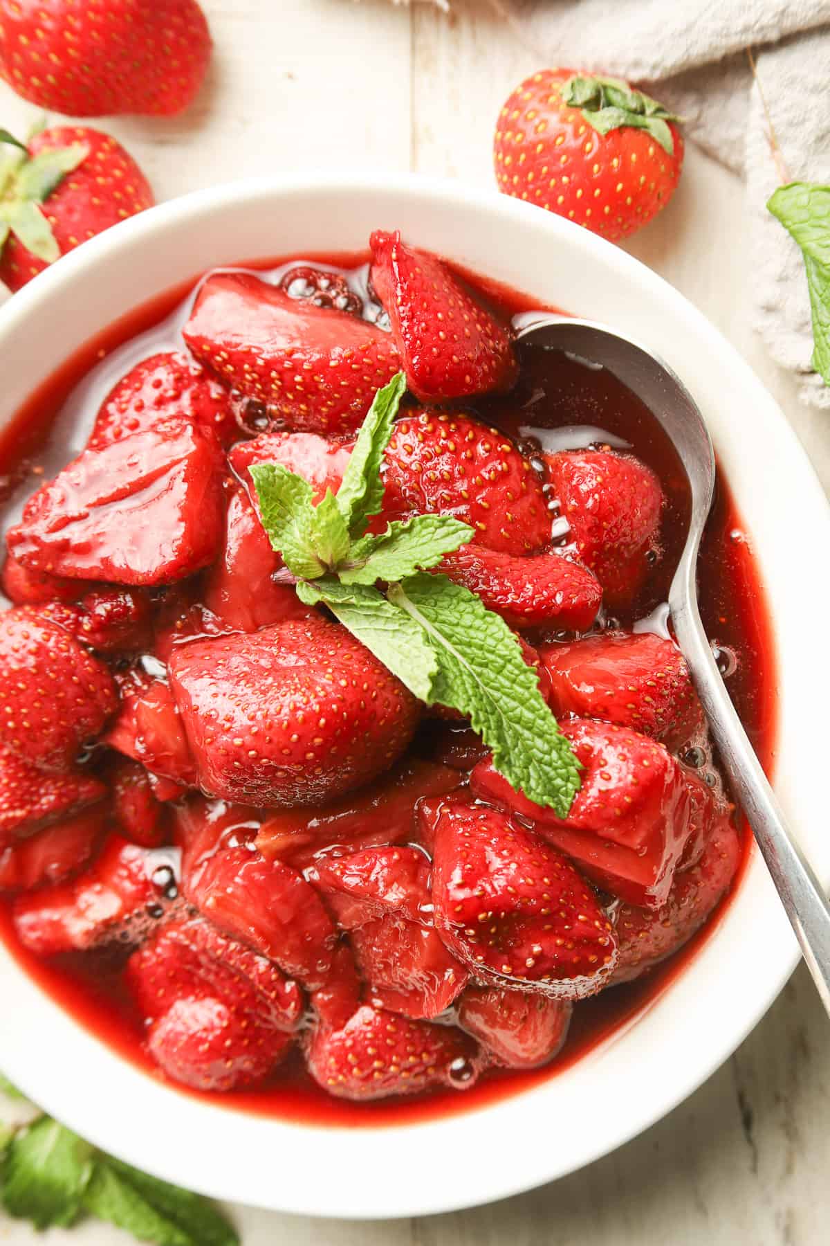 Close up of a bowl of Roasted Strawberries with fresh mint and a spoon.