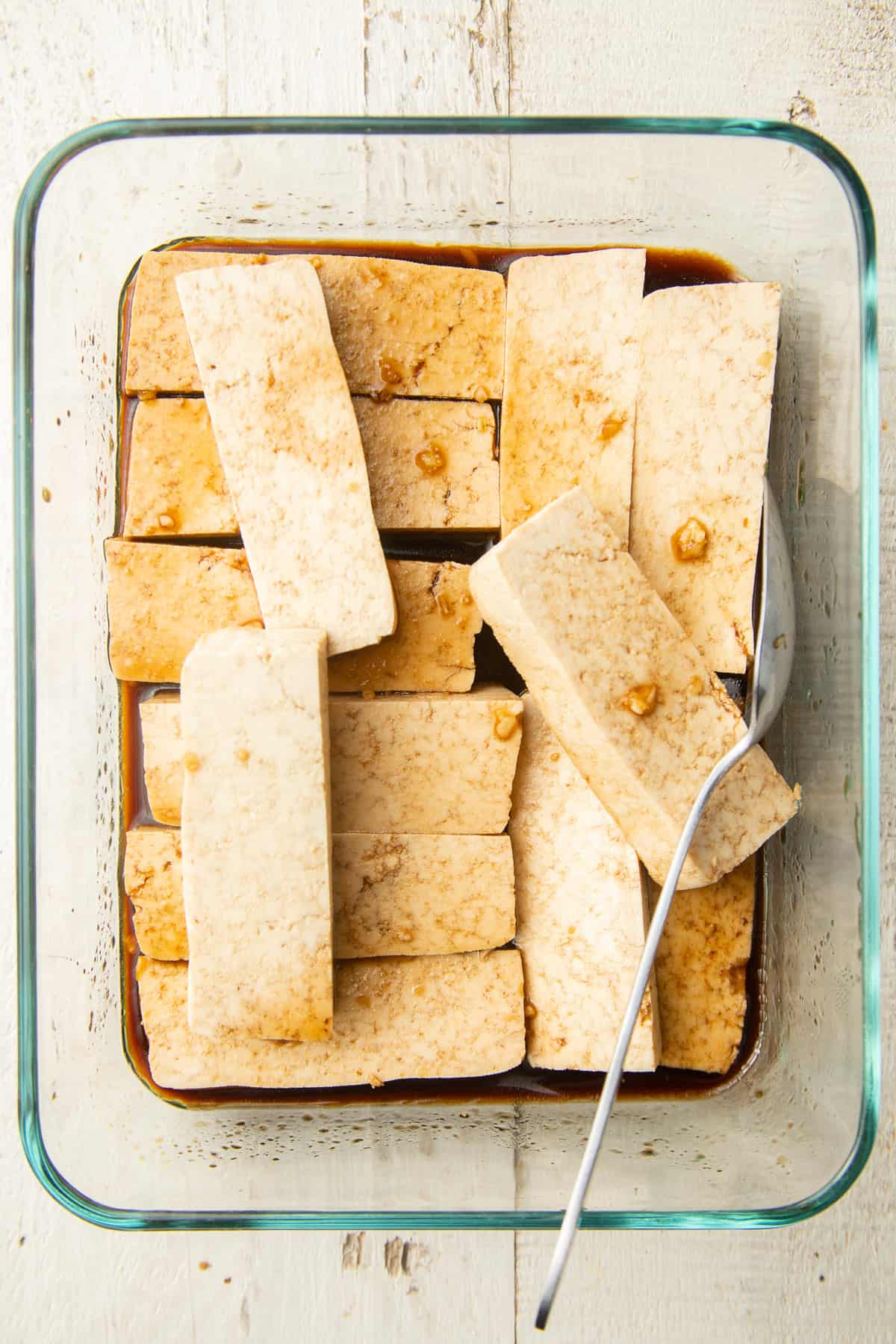 Tofu slices marinating in a dish.