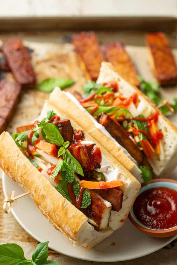Tofu Banh Mi on a plate with slices of baked tofu in the background.