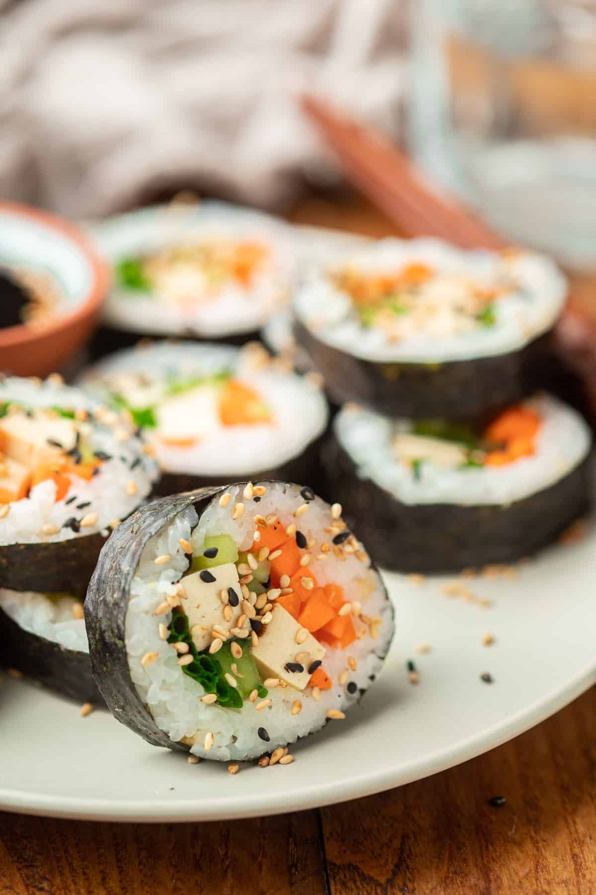 Close up of one slice of a tofu sushi roll on a plate, with additional pieces in the background.