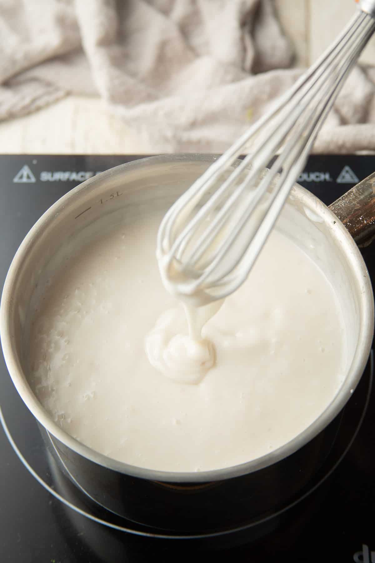 Whisk drizzling cooked coconut pudding into a saucepan.