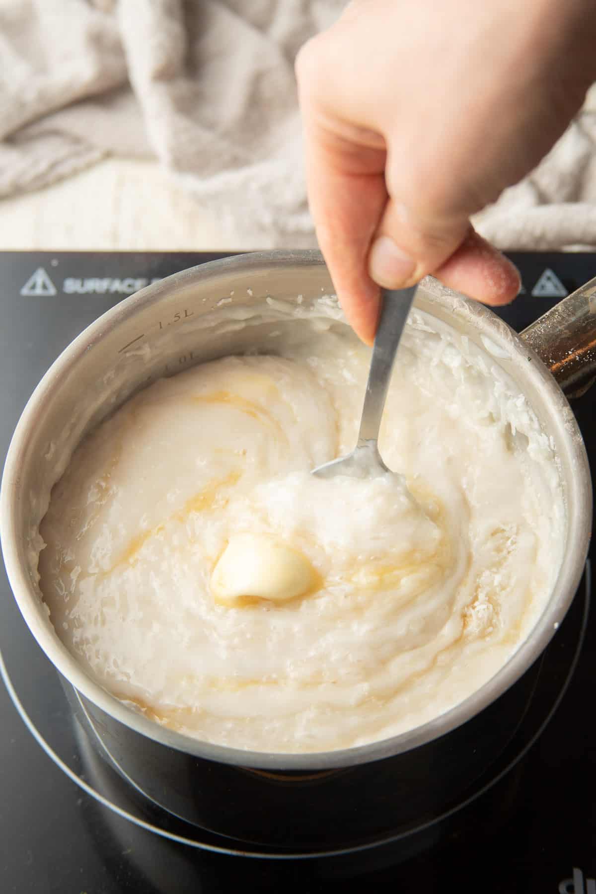 Hand stirring coconut and vegan butter into coconut cream pie filling.