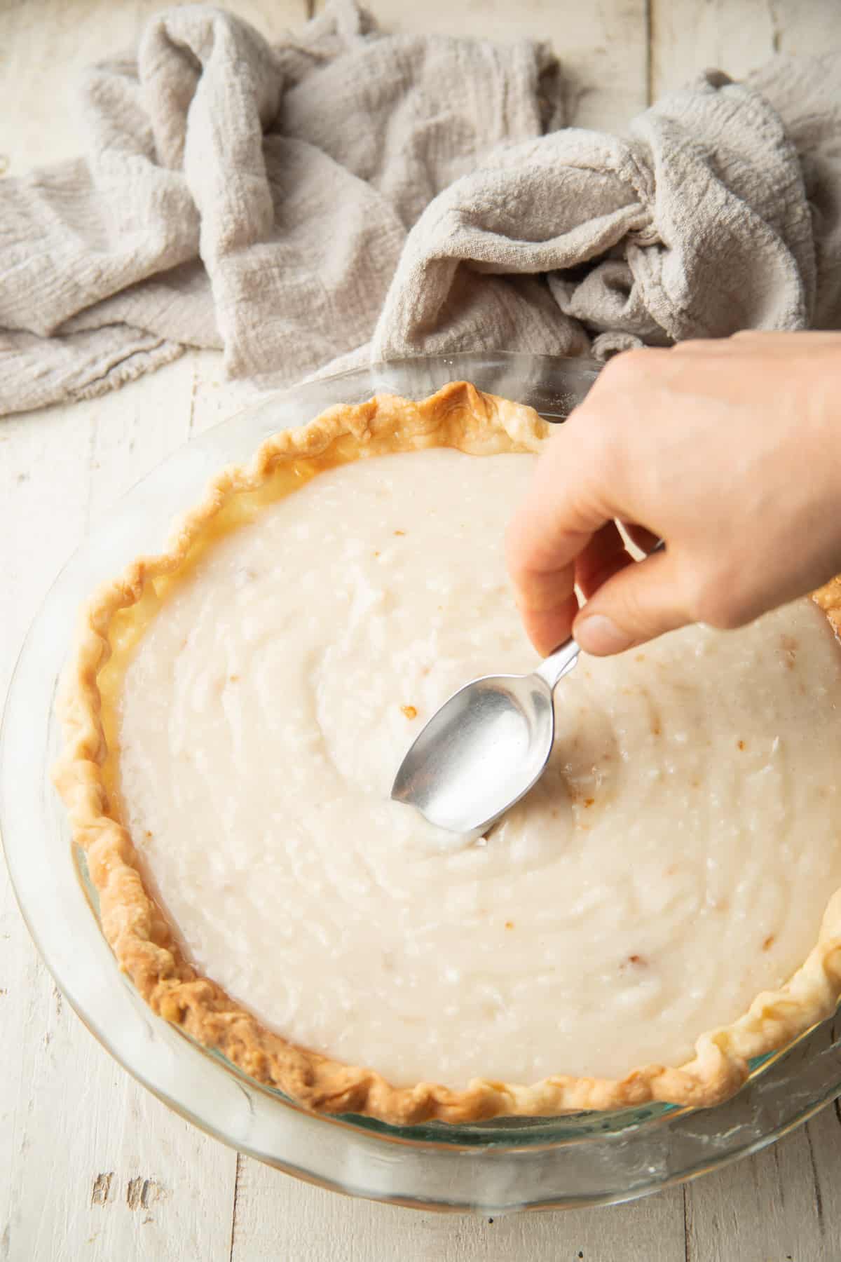 Hand with spoon smoothing out Vegan Coconut Cream Pie filling in a crust.