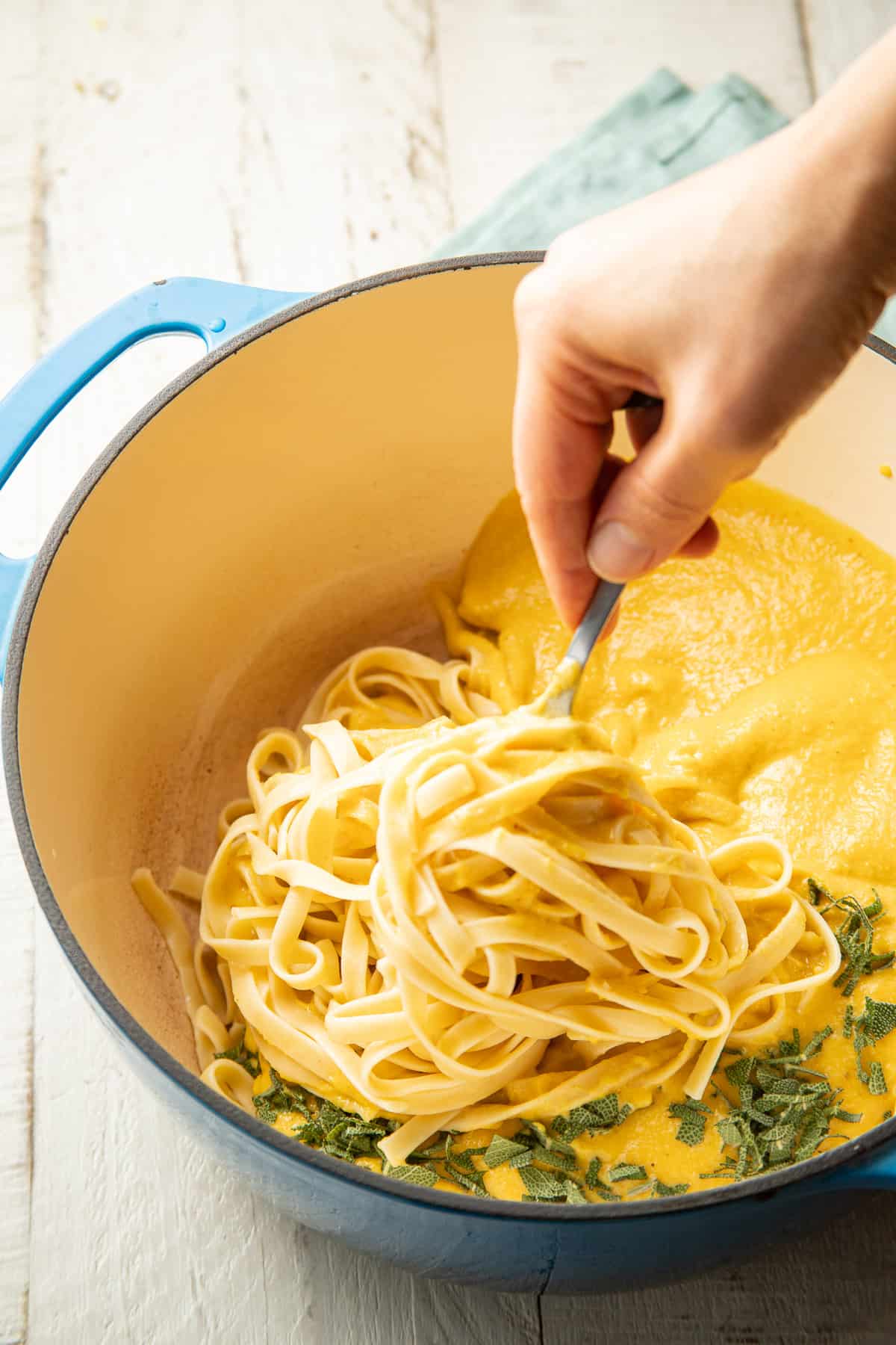 Hand stirring butternut squash sauce and sage into a pot of fettuccine.