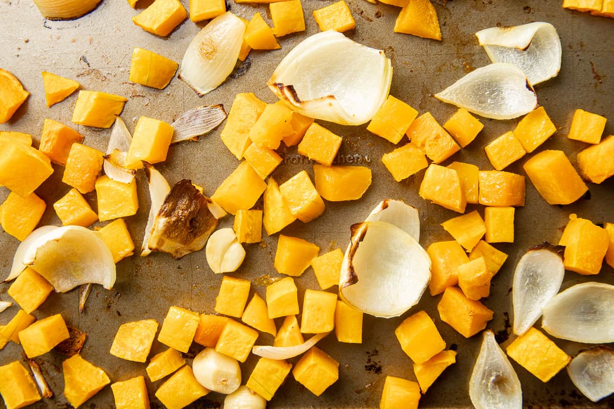 Roasted butternut squash, onions and garlic on a baking sheet.