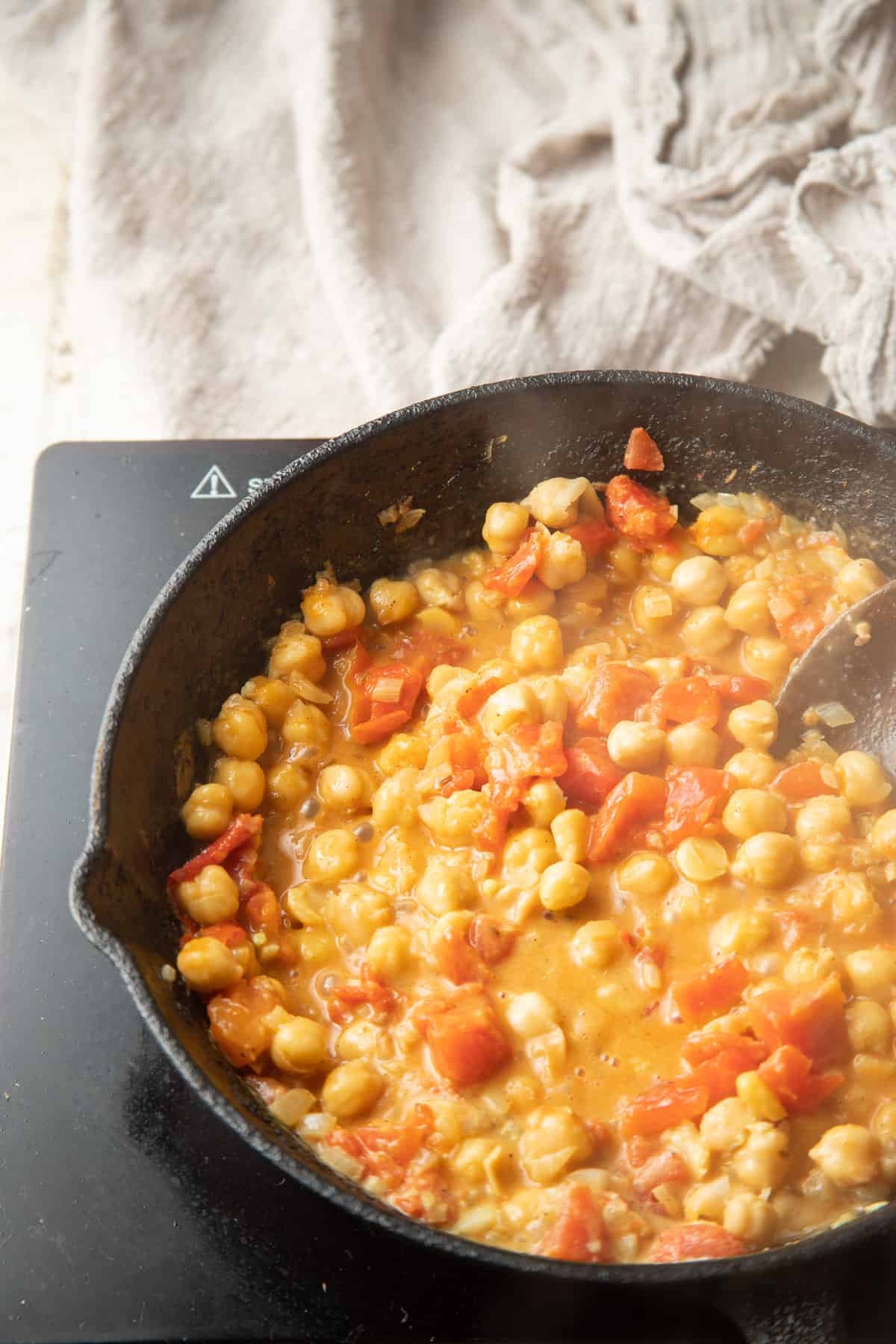 Chickpeas, tomatoes and coconut milk simmering in a skillet.