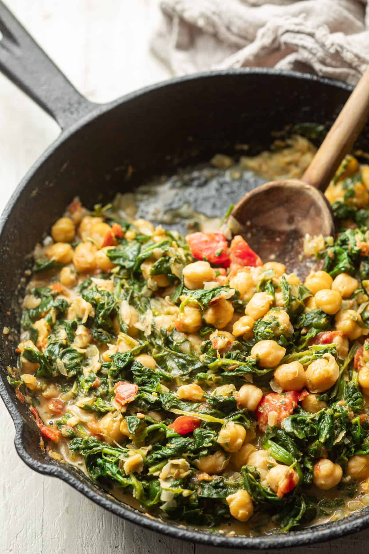 Skillet of Chickpea & Spinach Curry with a wooden spoon in it.