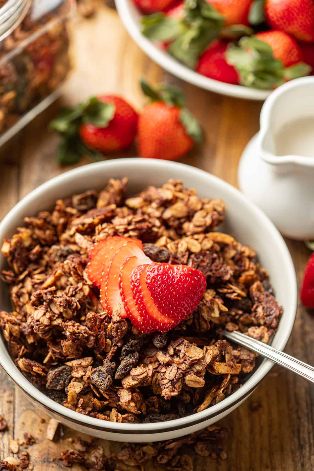 Bowl of Chocolate Granola with almond milk and strawberries in the background.