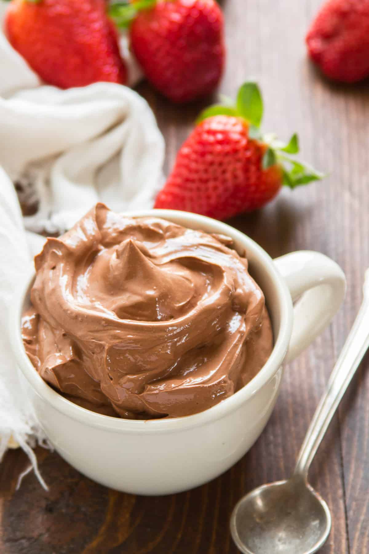 Cup of Vegan Chocolate Pudding with strawberries in the background.