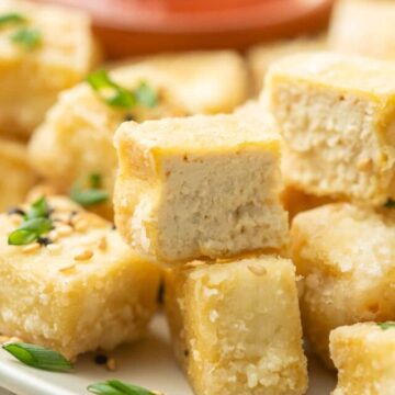 Close up of a half of a piece of Fried Tofu on a plate with additional fried tofu cubes.