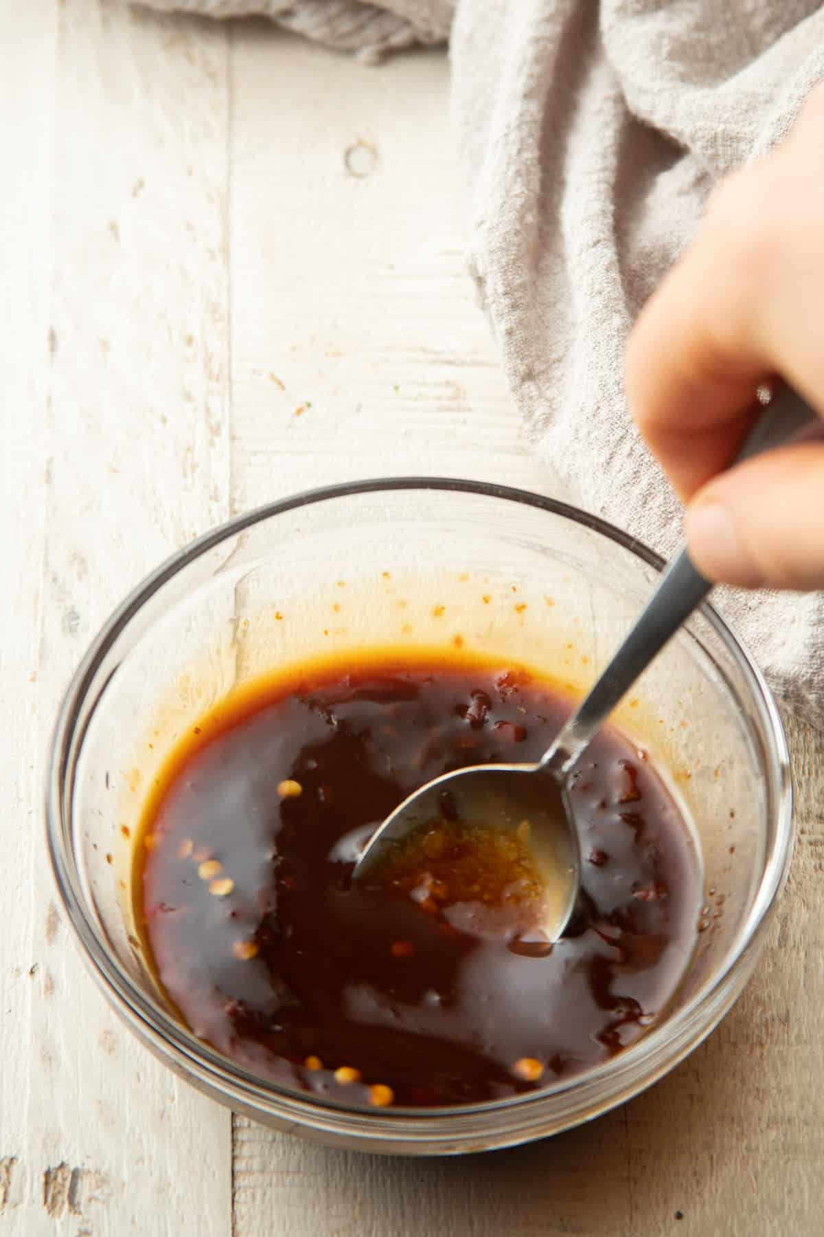 Hand stirring sauce ingredients for Vegan Drunken Noodles together in a glass bowl.