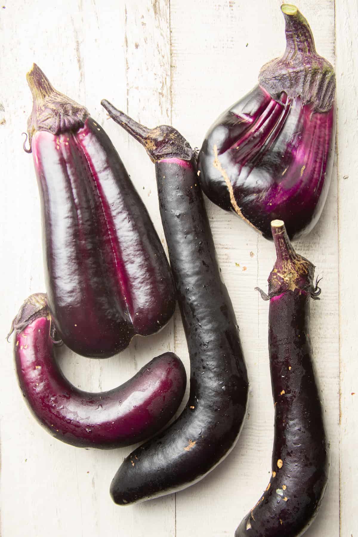 Five Japanese eggplants on a white wooden surface.