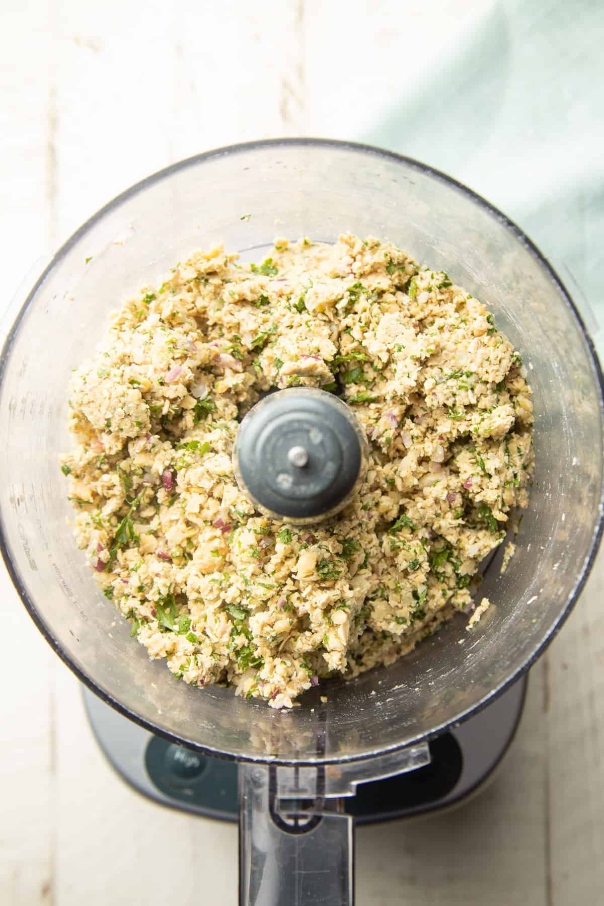 Ground chickpeas, oats, herbs, and spices in a food processor bowl.