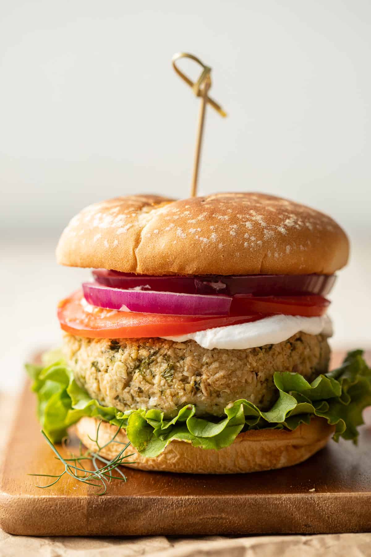 Falafel burger on a bun with lettuce, tomato, vegan yogurt, and onion slices.