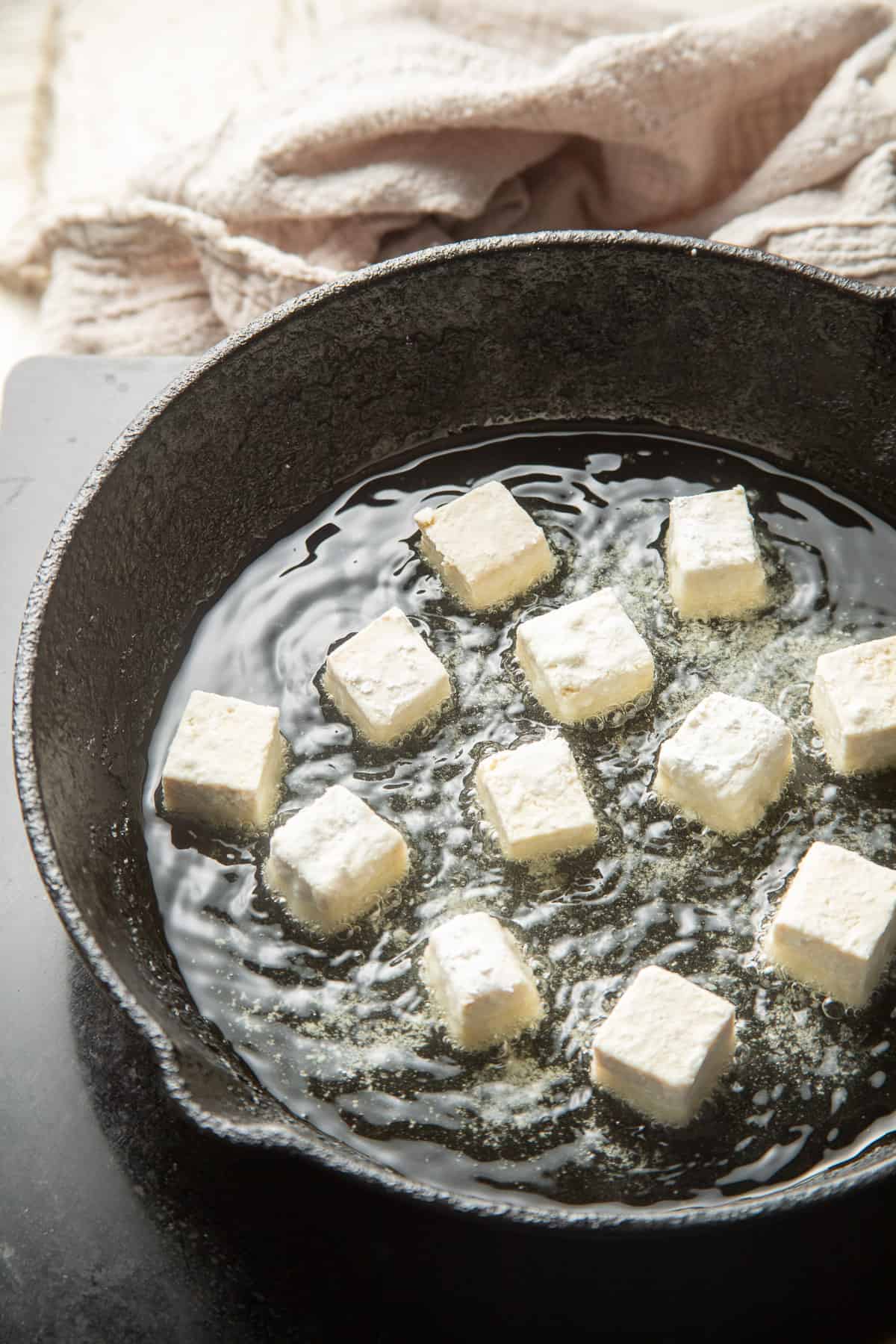 Tofu cubes coated in cornstarch in a skillet filled with oil.