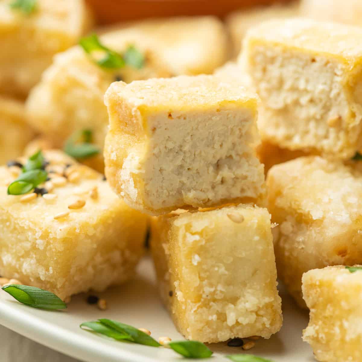 Close up of a piece of Fried Tofu cut in half on a plate with additional fried tofu pieces.