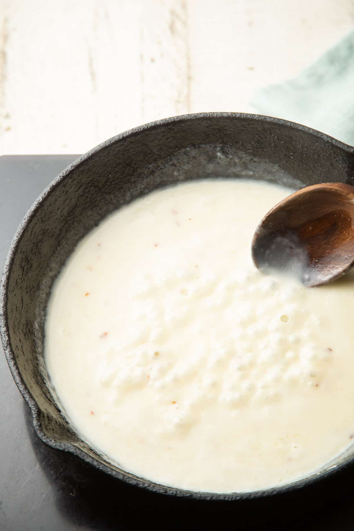 Creamy sauce cooking in a skillet with a wooden spoon.