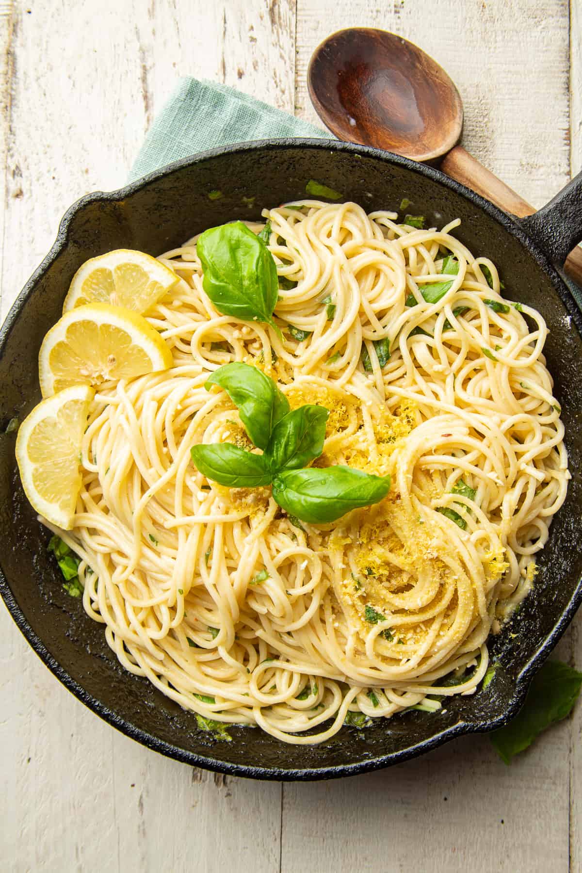 White wooden surface set with skillet of Lemon Pasta and wooden spoon.