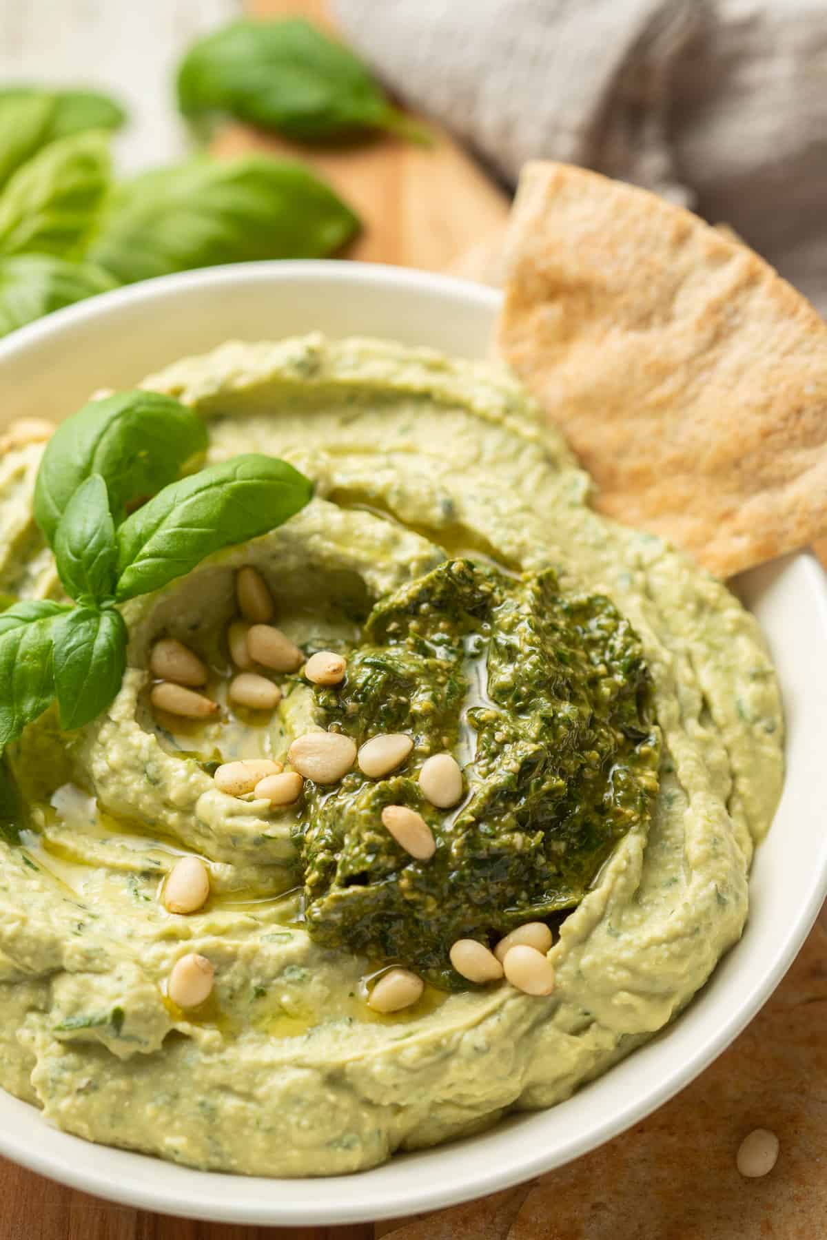 Bowl of Pesto Hummus with a pita wedge in it.