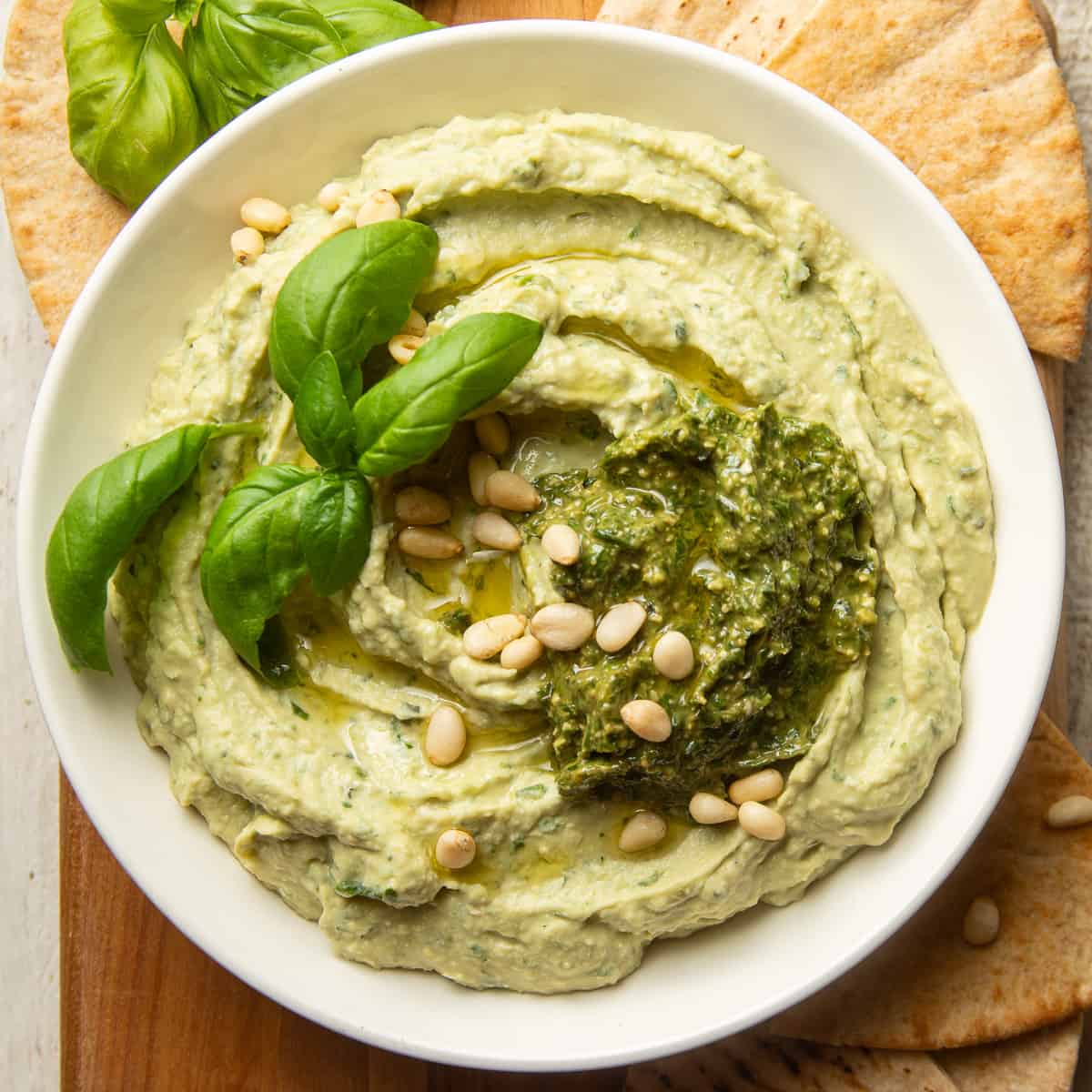 Pesto Hummus in a bowl topped with pine nuts, pesto, and basil leaves.