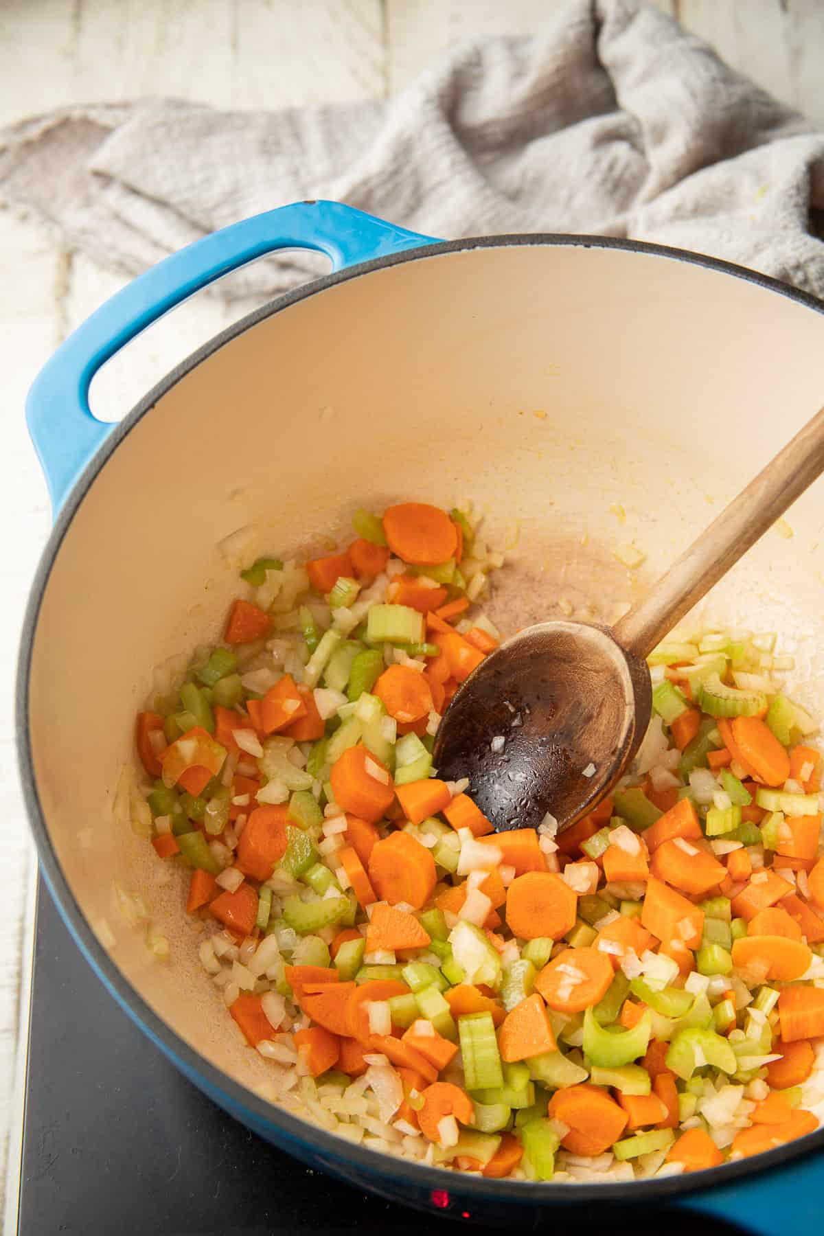 Onions, carrots and celery cooking in a pot with wooden spoon.