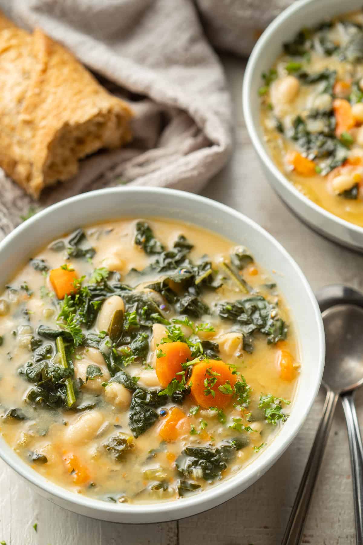 Two bowls of Tuscan Kale Soup with baguette in the background.
