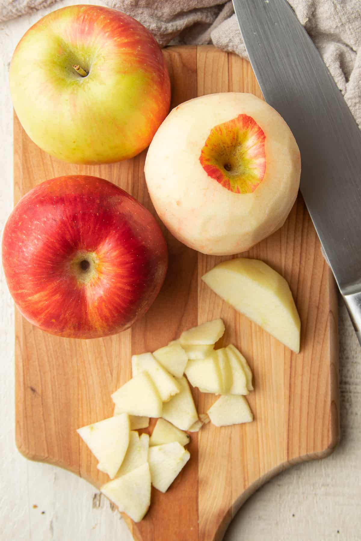 Two whole apples, one peeled apple, and apple slices on a cutting board with knife.