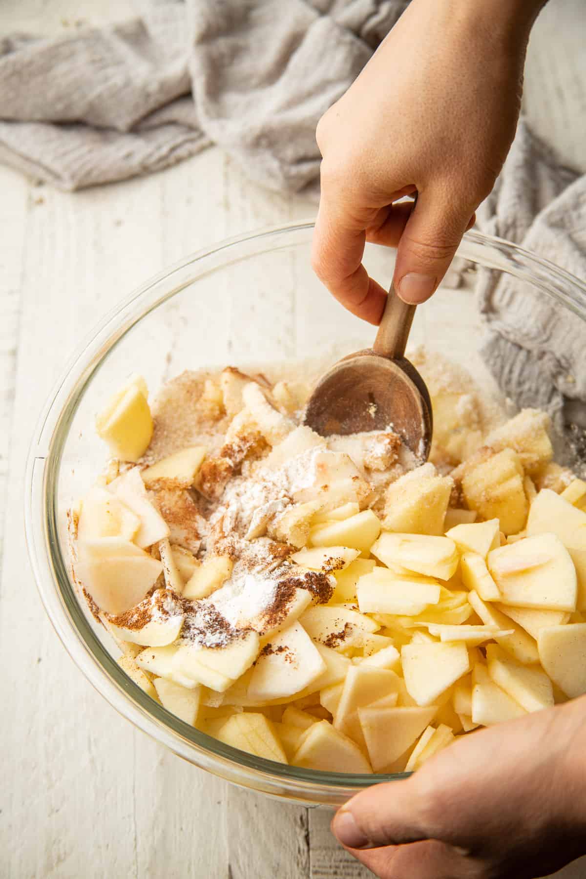 Hands stirring vegan apple pie filling together in a bowl.