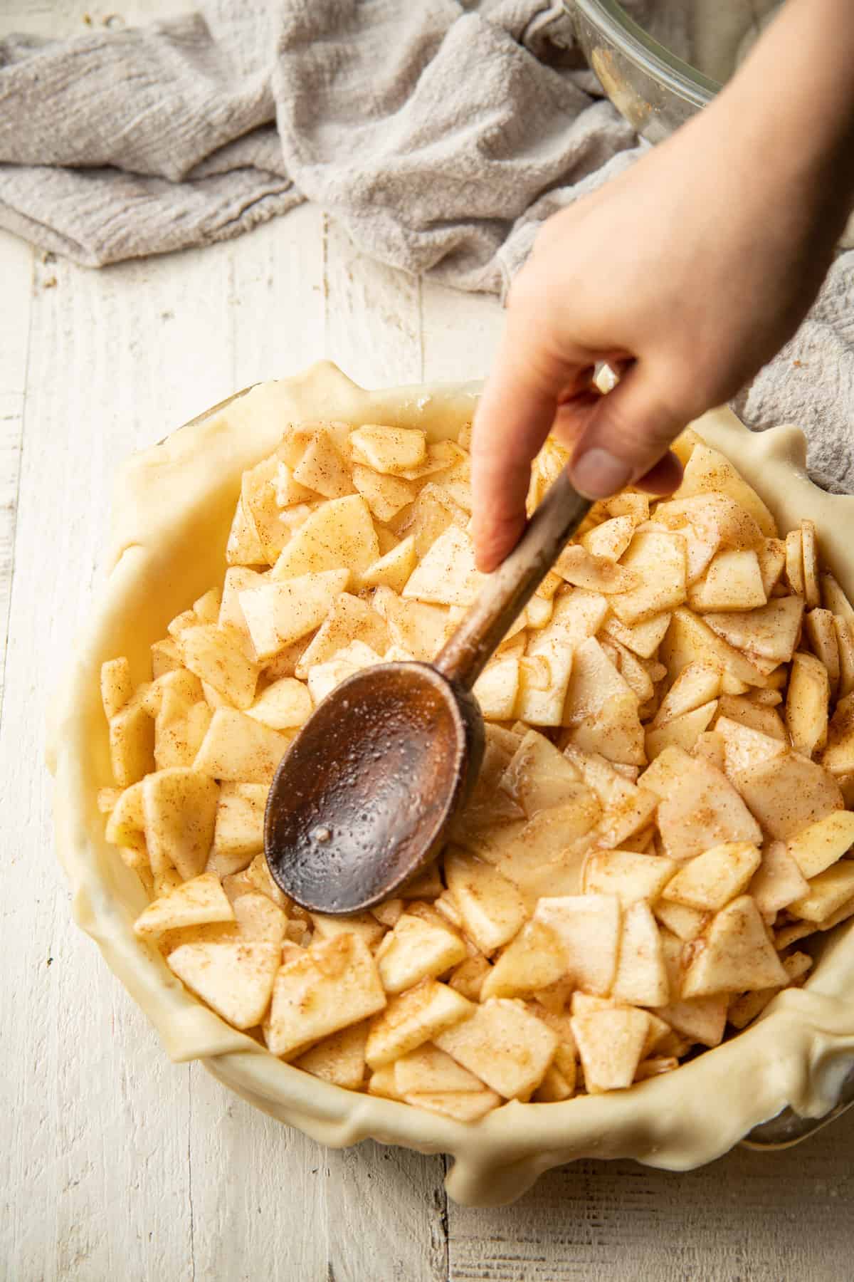 Hand using a wooden spoon to pack vegan apple pie filling into a crust.