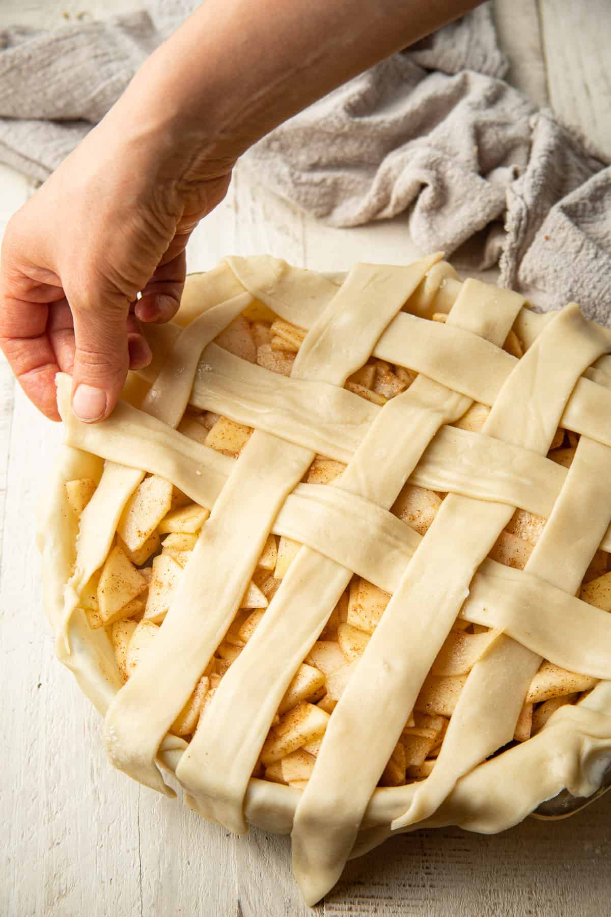 Hands arranging pie crust strips in a lattice formation.