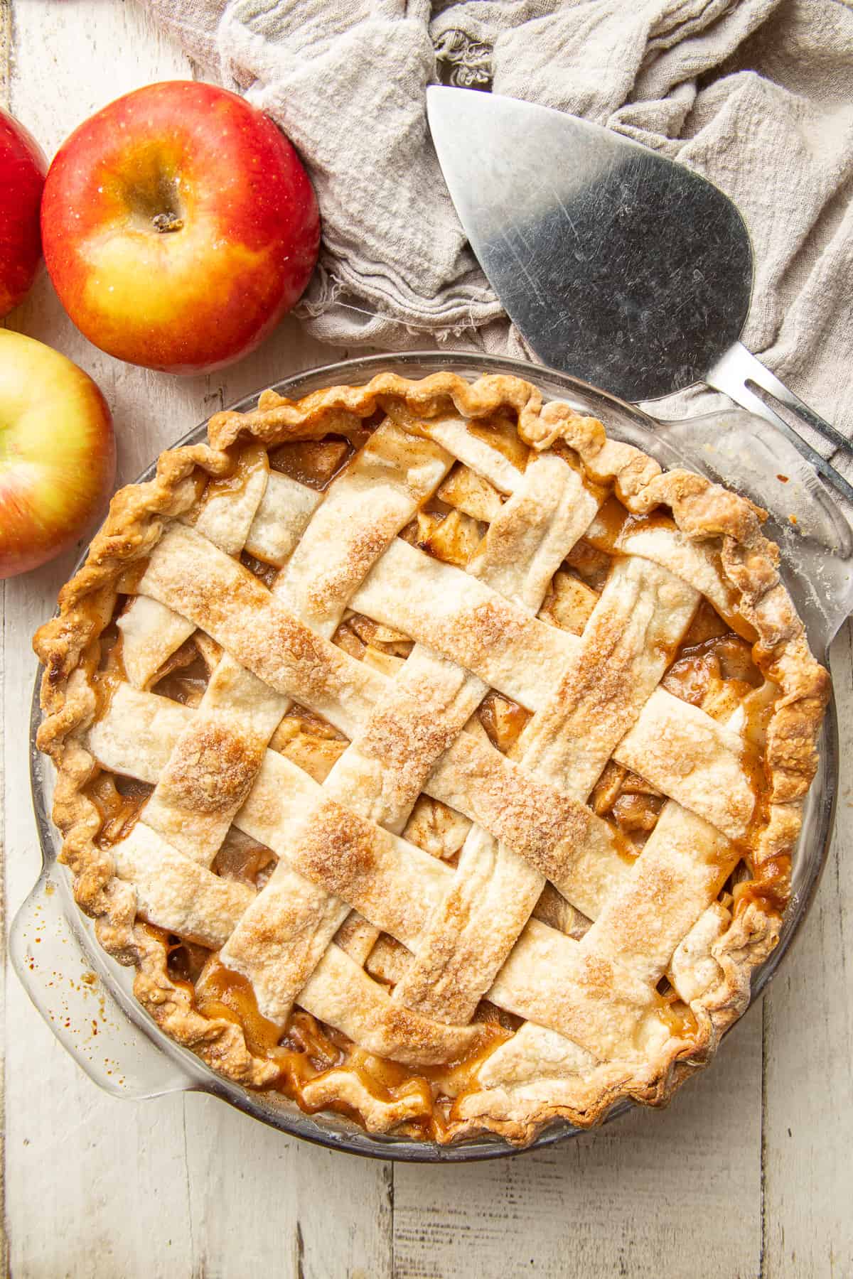 Whole vegan apple pie with pie server and apples on the side.