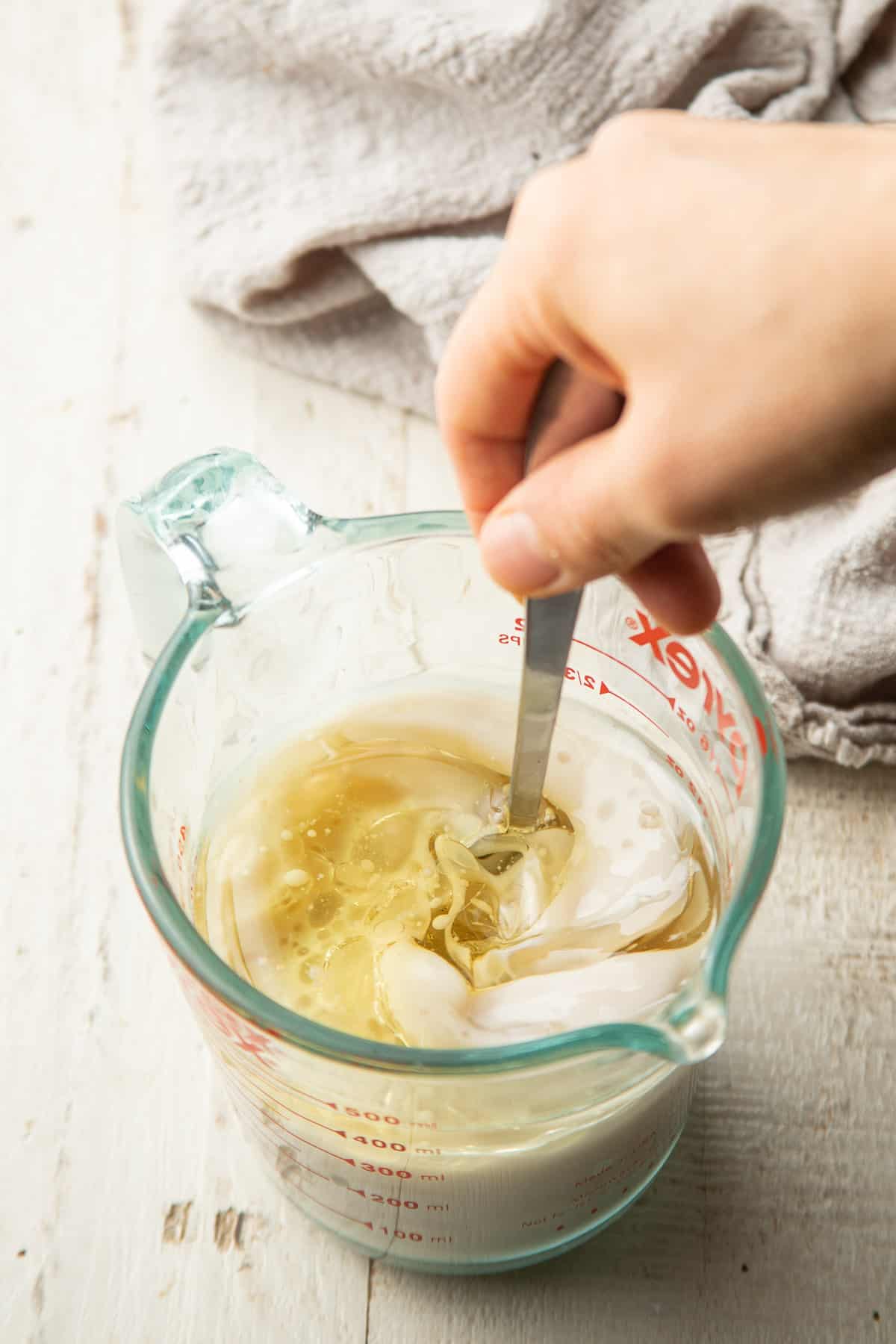Hand stirring oil into a measuring cup filled with non-dairy milk.