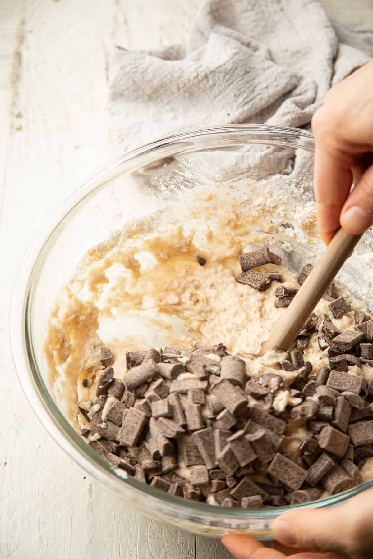 Hand folding chocolate chunks into a bowl of muffin batter.