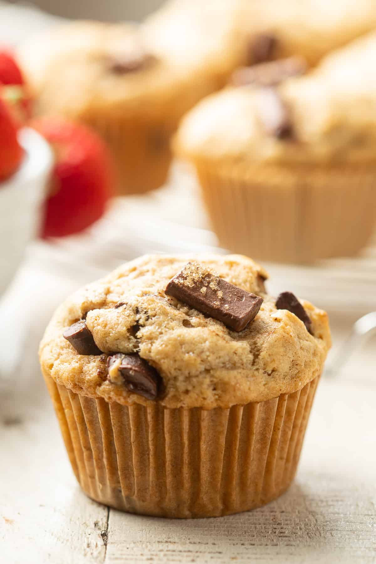 Vegan Chocolate Chip Muffin with additional muffins and strawberries in the background.