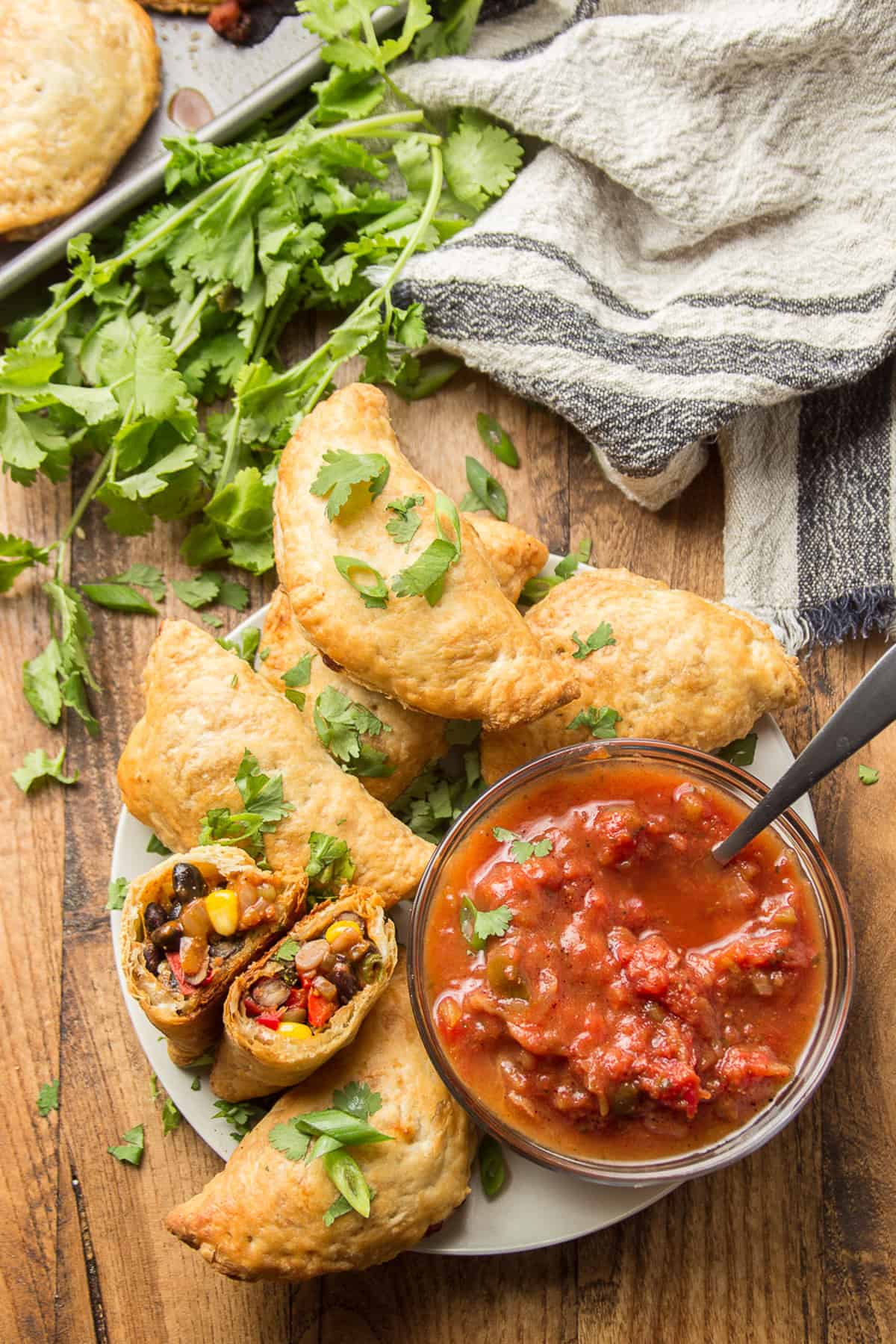 Wooden surface set with a plate of Vegan Empanadas and dish of salsa.