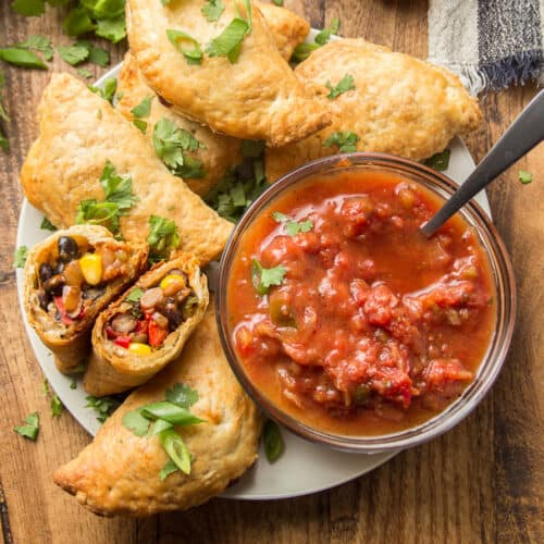 Vegan Empanadas on a plate with salsa, one empanada cut in half to show fillings.